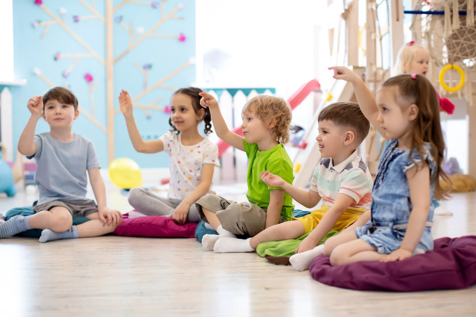 A group of children sitting together on floor cushions in a bright playroom