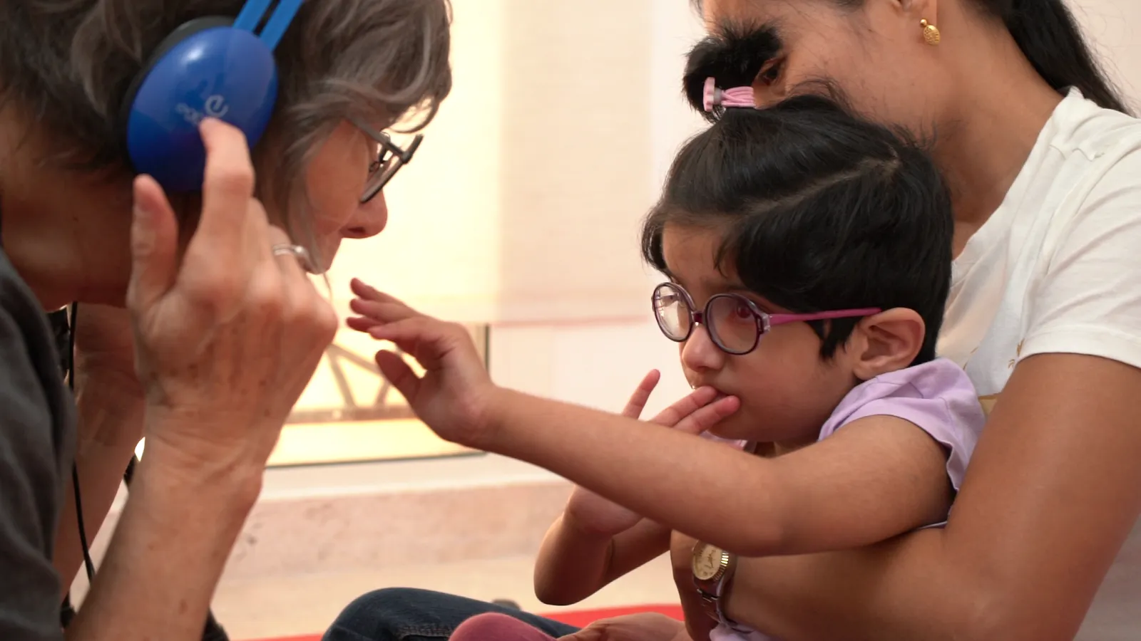 A child explores a listening activity with headphones alongside a therapist and parent