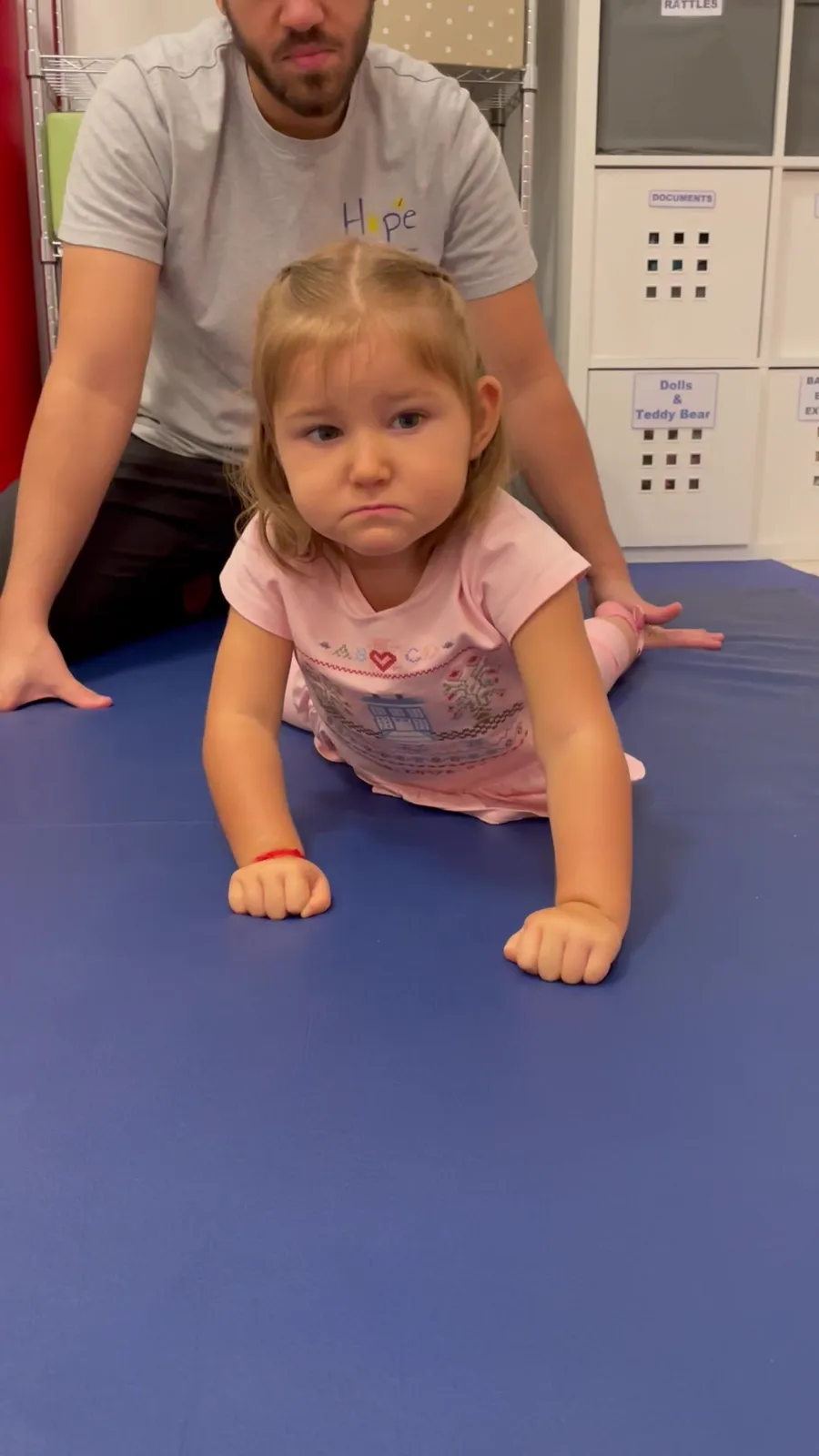 A therapist supports a toddler crawling on a mat