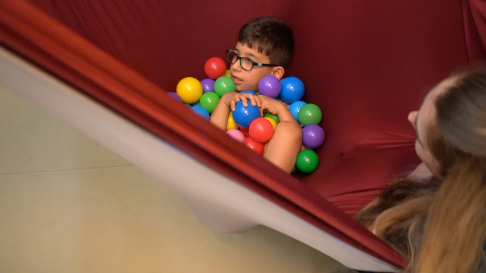 A child plays among colorful balls in a sensory hammock