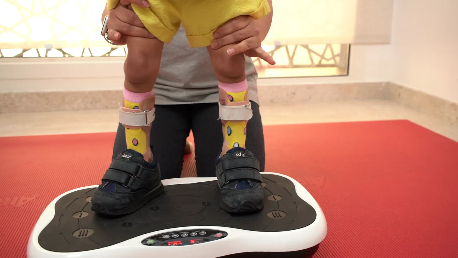 A therapist supports a child standing on a vibration platform