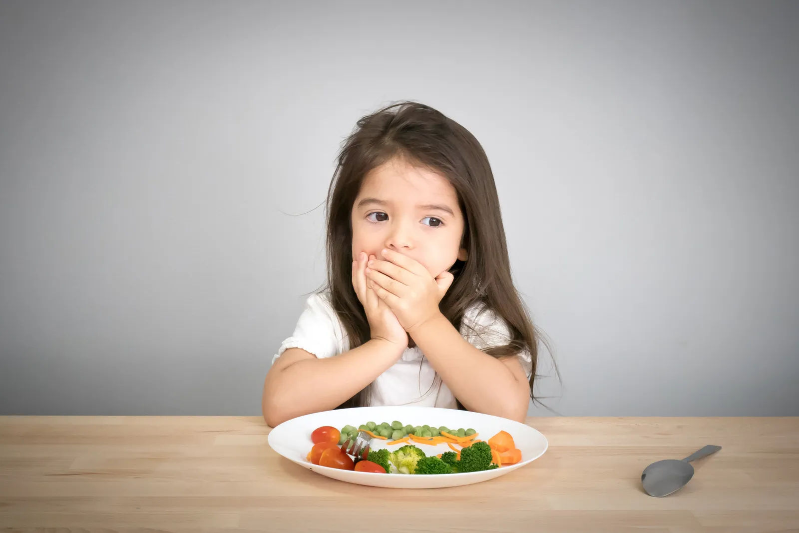 A girl covers her mouth in front of a plate of vegetables