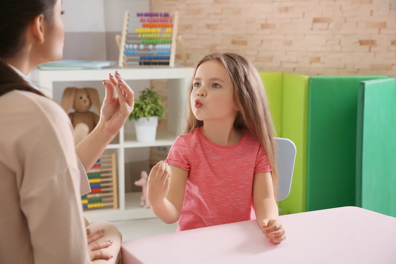 A speech therapist works face to face with a girl