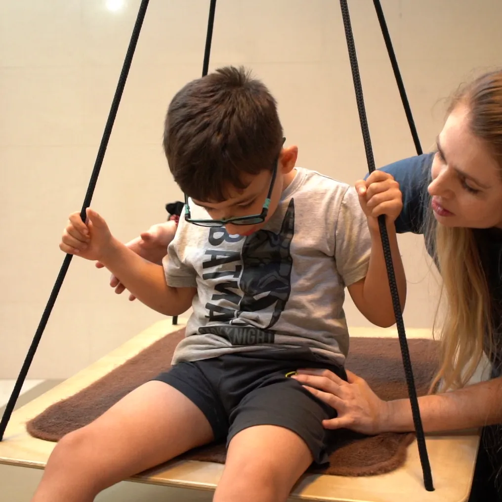 A Hope therapist supports a boy as he sits on a therapy swing