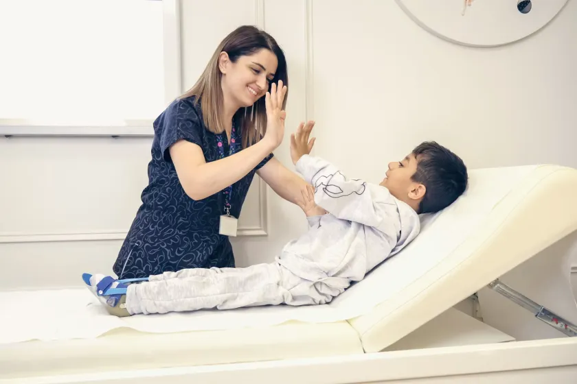 A nurse shares a high five with a boy resting on an adjustable bed