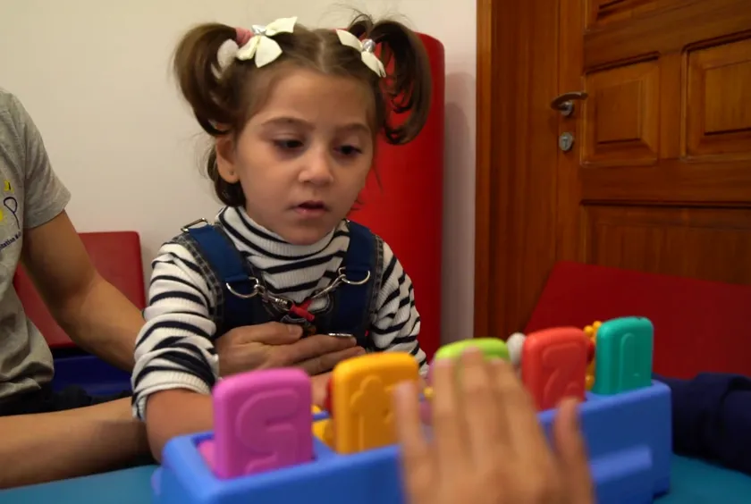 A girl plays with colorful letter blocks as her therapist guides her