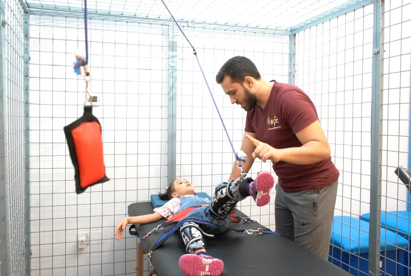 A physiotherapist supports a child lying on a therapy bench in a suspension frame