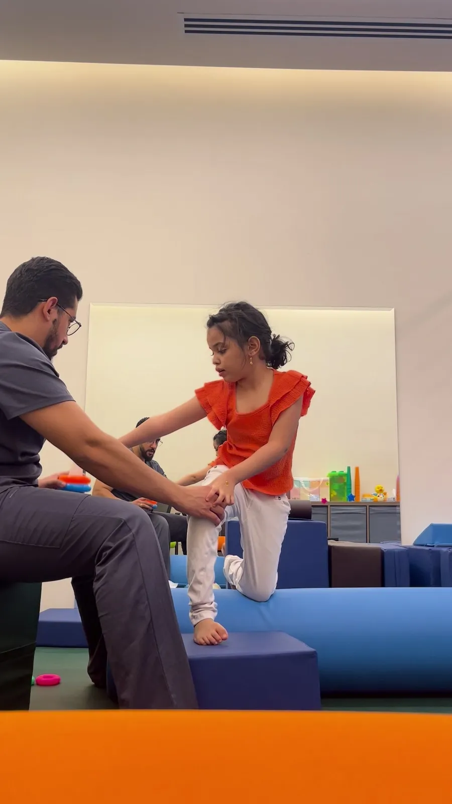 A therapist supports a girl reaching during an exercise