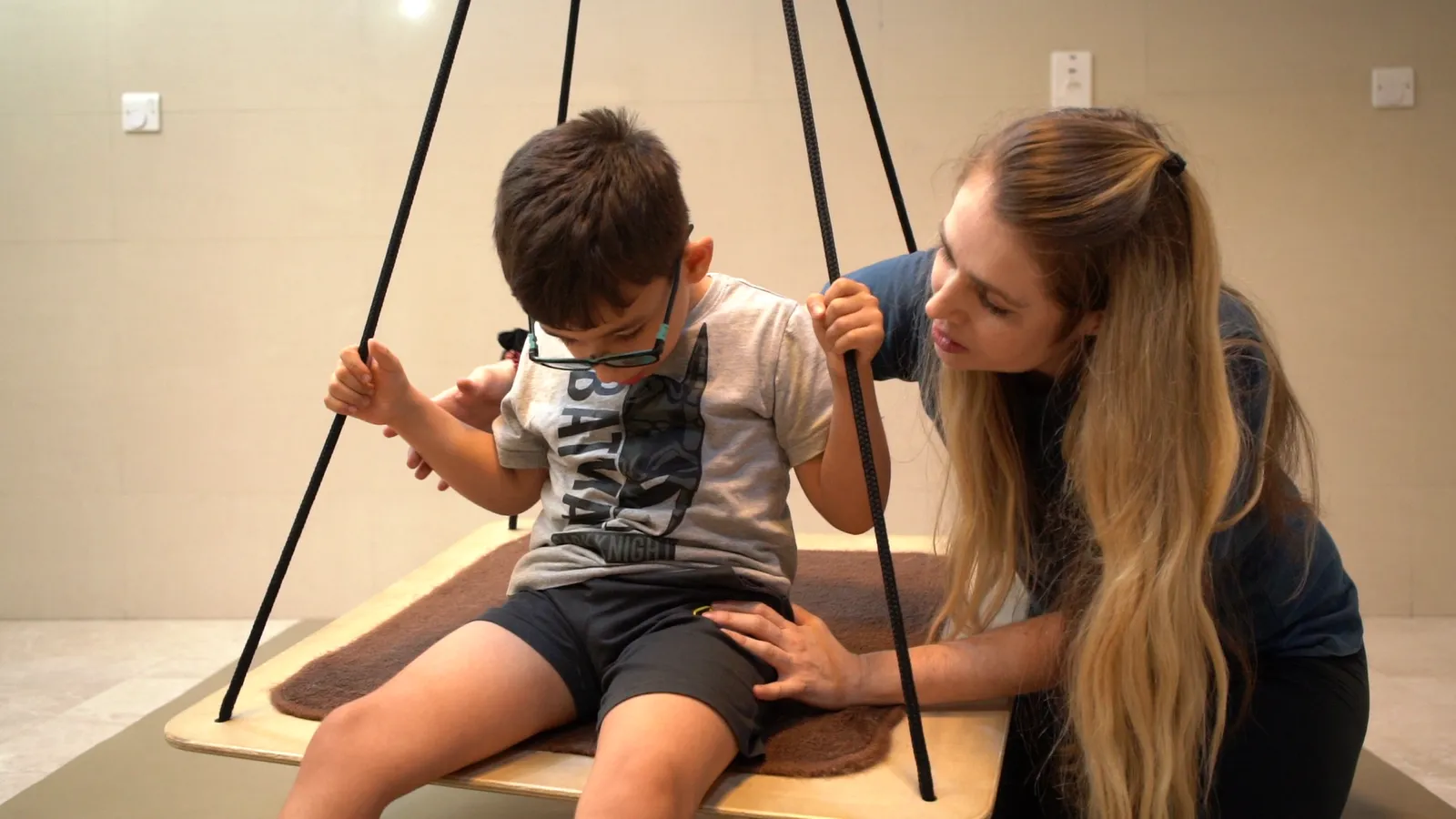 A therapist supports a child on a platform swing