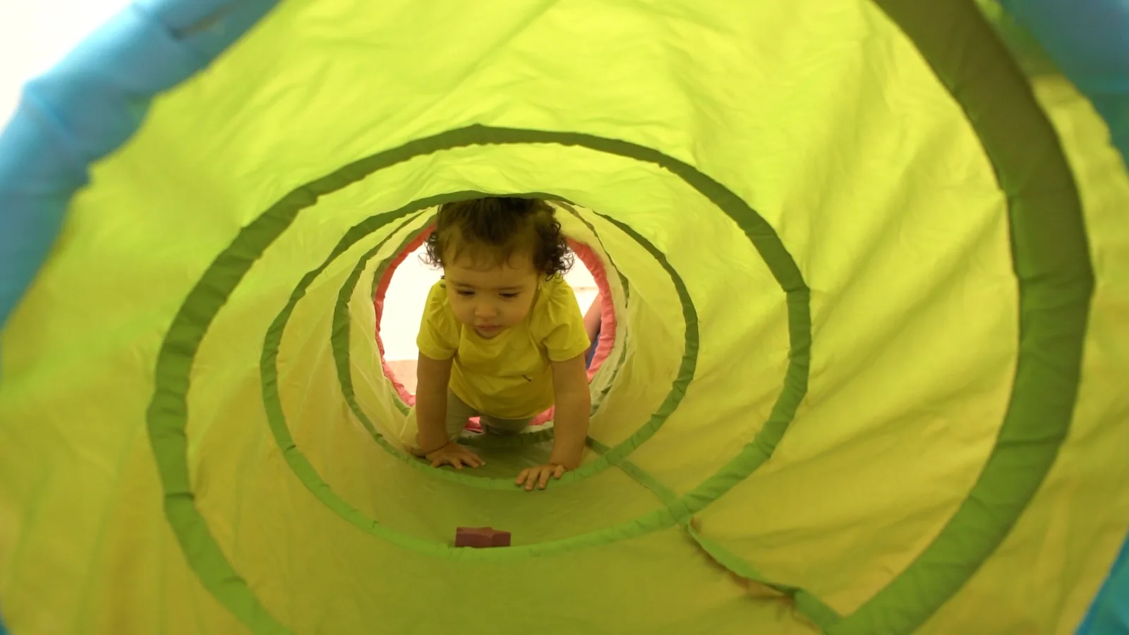A smiling toddler crawling through a play tunnel at Hope